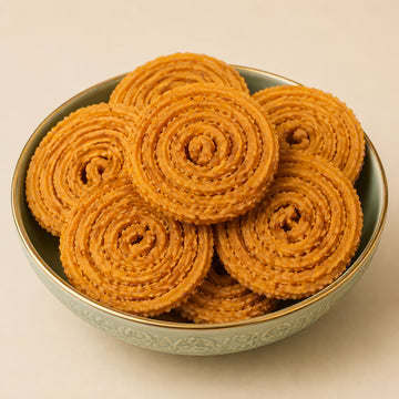 MM Mithaiwala Bada Chakli, golden spiral-shaped snacks stacked in a decorative bowl against a beige background.