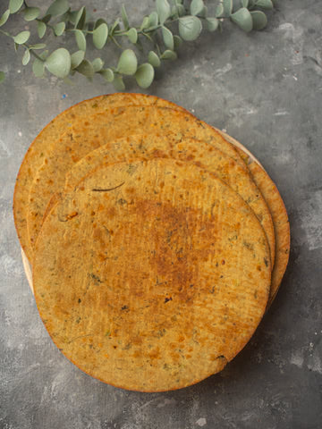 MM Mithaiwala Bada Khakhara, large round golden crisps stacked on a grey surface with green leaves.
