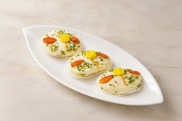 MM Mithaiwala Badam Milan garnished with almonds and pistachios, arranged on a white leaf-shaped platter.