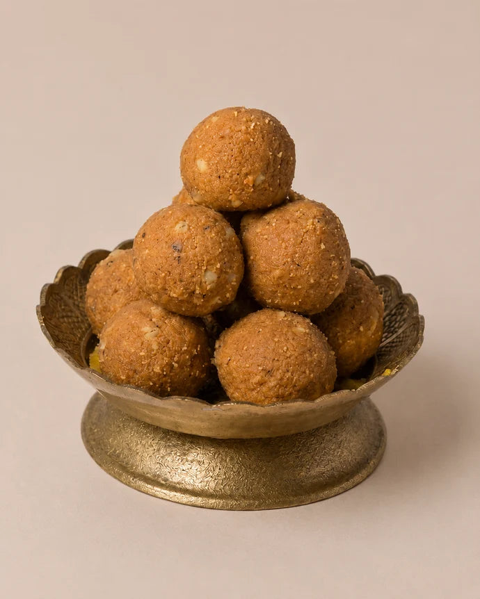 MM Mithaiwala Besan Laddu with visible nut pieces, stacked in a decorative brass pedestal bowl against a beige background.