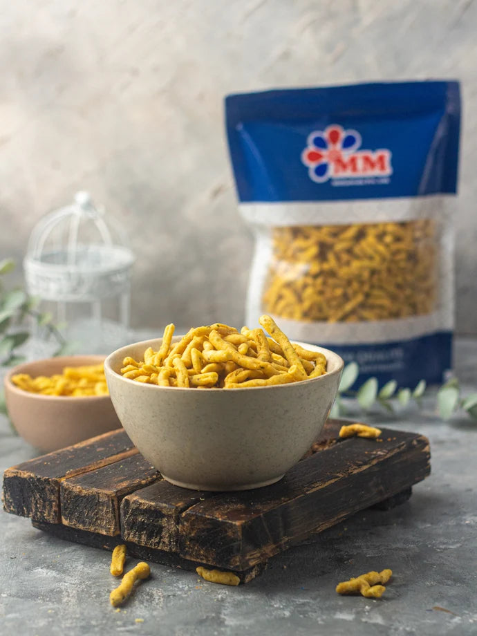 MM Mithaiwala Bhavnagari Gathiya served in a bowl on a wooden board, with a branded blue pouch in the background.