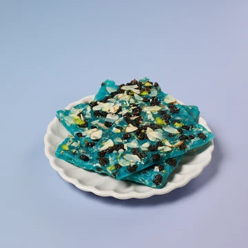 MM Mithaiwala Blueberry Ice Halwa topped with sliced nuts and dried fruit, stacked on a white scalloped plate.