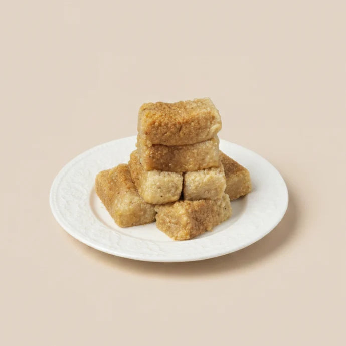 MM Mithaiwala Cake Barfi pieces stacked on a white patterned plate against a plain beige background.