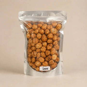 MM Mithaiwala Caramel Makhana in a silver resealable pouch with a clear front, against a beige background.