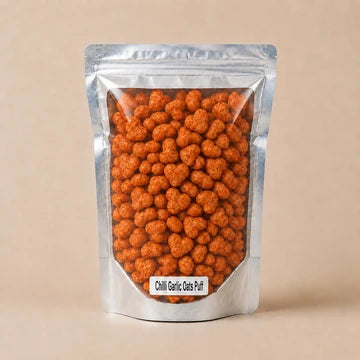 MM Mithaiwala Chilli Garlic Oats Puffs in a silver pouch showing reddish-orange seasoned puffs through its clear front.