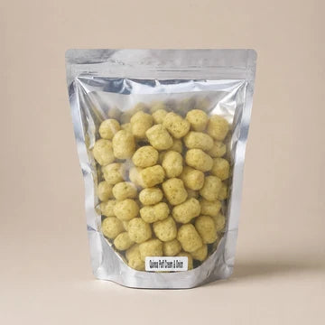 MM Mithaiwala Cream and Onion Quinoa Puffs in a silver pouch with a clear front, against a beige background.