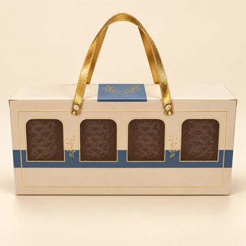 MM Mithaiwala Cream Gift Carrier with golden ribbon handles, a blue band and four clear front windows.
