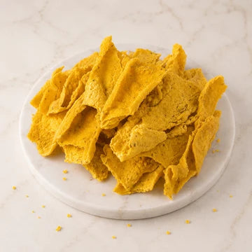 MM Mithaiwala Fafda, golden strips piled on a round white marble board against a light marble background.