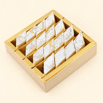 MM Mithaiwala Kaju Katli Box with diamond-shaped kaju katli topped with silver leaf in a gold tray.