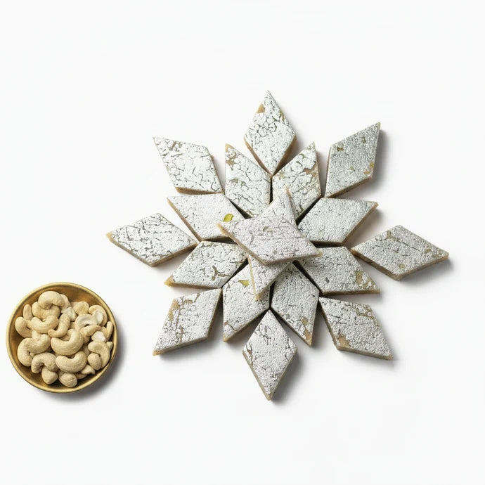 MM Mithaiwala Kaju Katli topped with silver leaf, stacked on a cream plate with cashews alongside.
