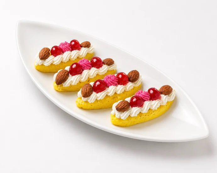 MM Mithaiwala Kashmir Ki Kali sweets topped with white and pink cream, red cherries and almonds, arranged against a golden background.