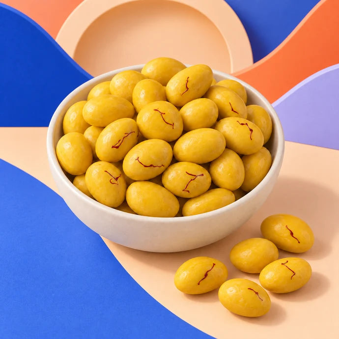 MM Mithaiwala yellow Kesar Draggies garnished with saffron strands, served in a white bowl.