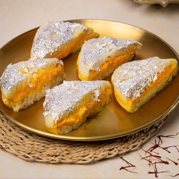 MM Mithaiwala Kesar Malai Sandwich topped with silver leaf, showing saffron-coloured filling on a gold plate.