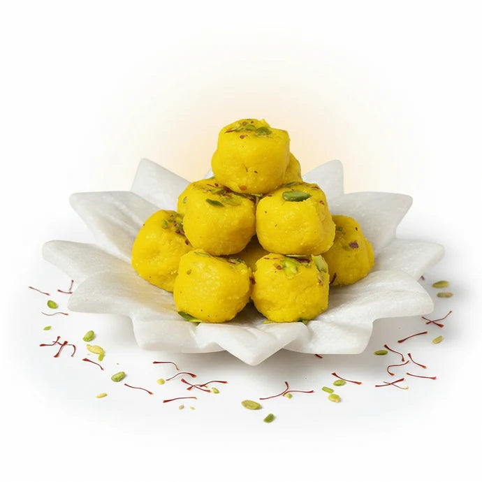 MM Mithaiwala Kesar Peda topped with pistachio slivers, stacked on a white flower-shaped plate with saffron strands scattered around.