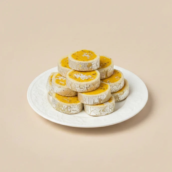 MM Mithaiwala round Malai Toast with yellow centres and silver leaf around the edges, stacked on a white patterned plate.