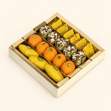 MM Mithaiwala Manthan Box with yellow and orange sweets alongside nut-covered mithai in a gold tray.