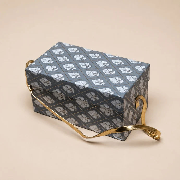 MM Mithaiwala Meethi Yaadein Box, a closed grey patterned gift box with a golden handle against a beige background.