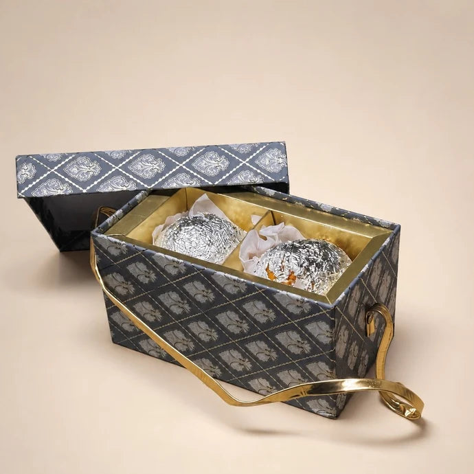 MM Mithaiwala Meethi Yaadein Box, a closed grey patterned gift box with a golden handle against a beige background.