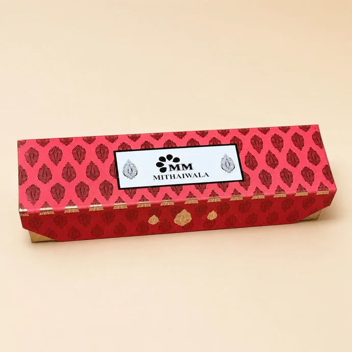 MM Mithaiwala Mithaas Box, a closed red gift box with traditional motifs and a branded label against a beige background.