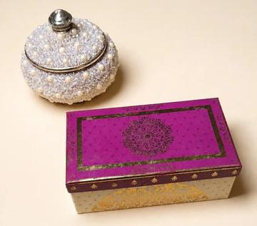 MM Mithaiwala Mithai Mood Box, a closed cream and gold gift box with a magenta patterned lid beside a decorative pearl-studded jar.