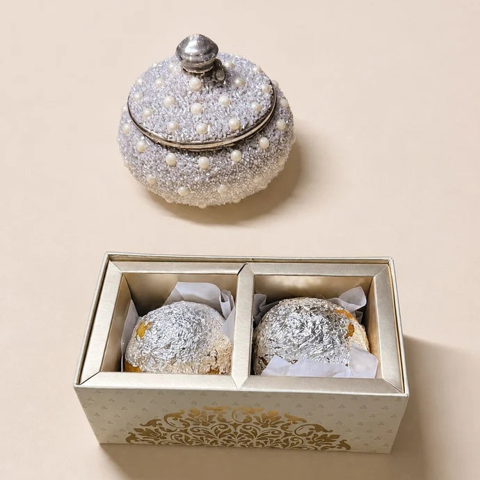 MM Mithaiwala Mithai Mood Box opened to reveal two silver-leaf-covered laddus in individual compartments beside a decorative jar.