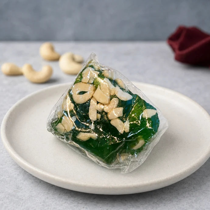 MM Mithaiwala green Badami Halwa piece from the 500g mix, topped with cashews and individually wrapped on a white plate.