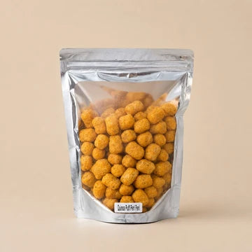 MM Mithaiwala Peri Peri Quinoa Puffs in a silver pouch showing orange-seasoned puffs through its clear front.