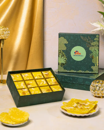 MM Mithaiwala Pineapple Ice Halwa Gift Box with a green botanical lid and twelve gold compartments, displayed with halwa and pineapple slices.