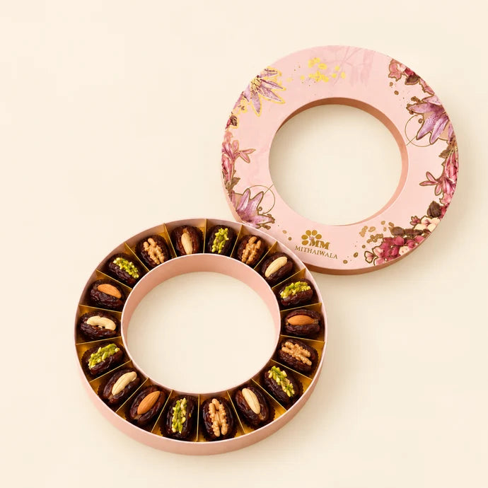 MM Mithaiwala Pink Crown Box opened to display stuffed dates arranged in a circle, with its floral lid behind.