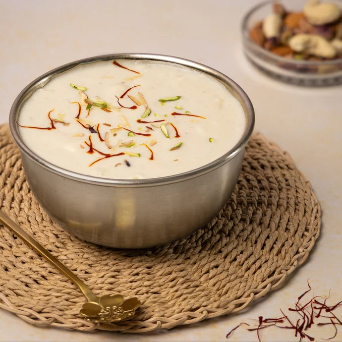 MM Mithaiwala Rabdi garnished with saffron, almonds and pistachios, served in a metal bowl on a woven placemat.