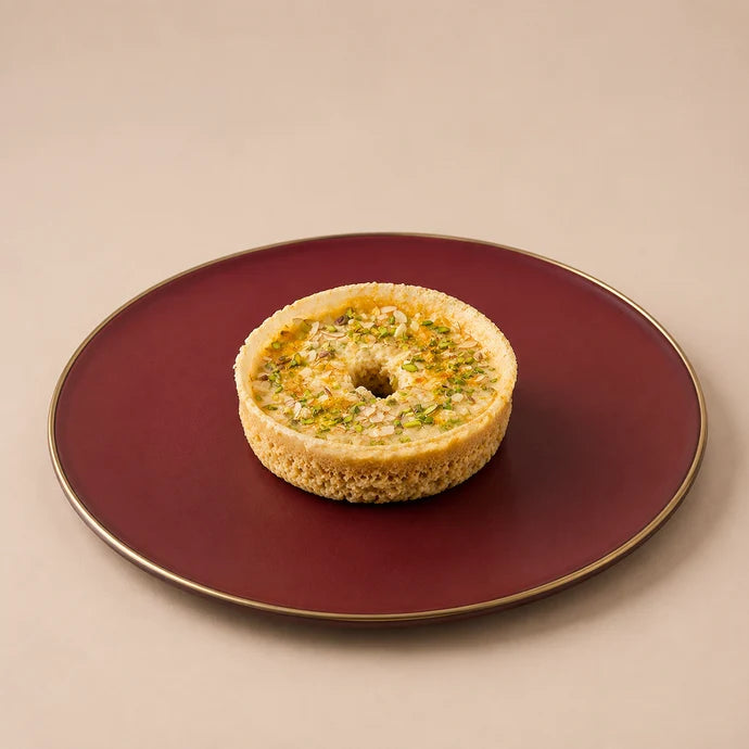 MM Mithaiwala Small Malai Ghevar topped with malai and chopped nuts, served on a maroon plate with a gold rim.