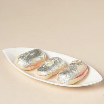 MM Mithaiwala Square Malai Sandwich topped with silver leaf, showing a pink filling on a white leaf-shaped platter.