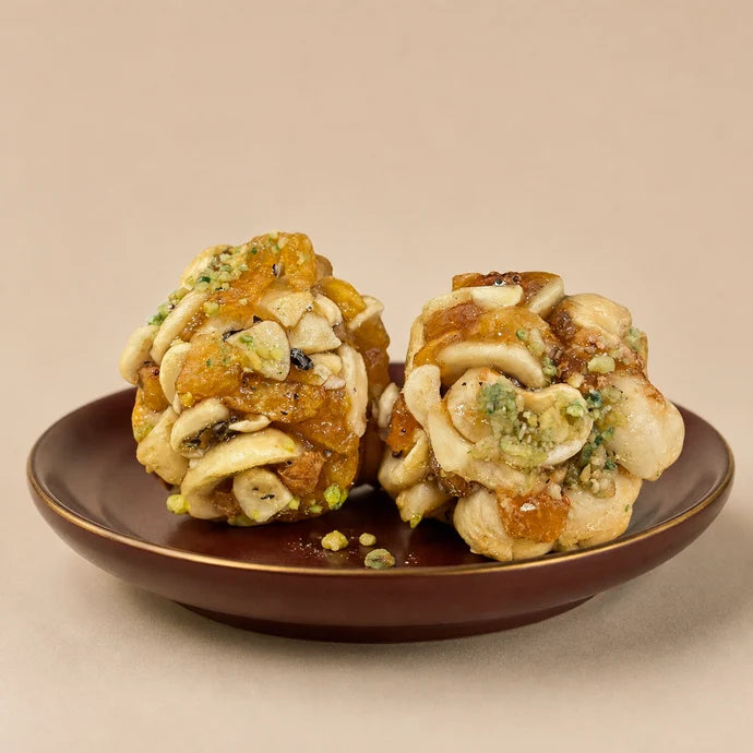 MM Mithaiwala Sugar Free Jardalu Laddu shown close up with cashews, apricot pieces and pistachio garnish on a maroon plate.