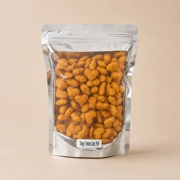 MM Mithaiwala Tangy Tomato Oats Puffs in a silver pouch with a clear front, against a beige background.