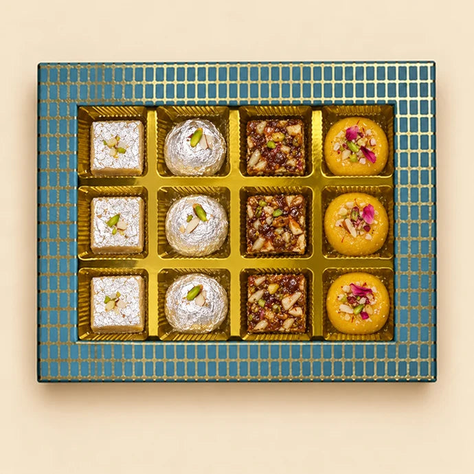 MM Mithaiwala The Pearl Edit Blue 12 Cavity Box with assorted sweets in golden compartments and a blue and gold grid-patterned border.