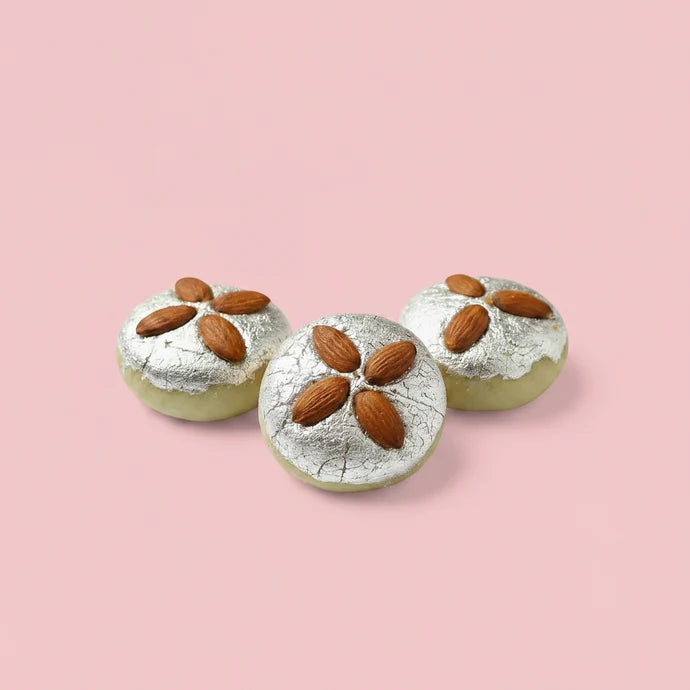 MM Mithaiwala Vaikunth Bhog sweets topped with silver leaf and whole almonds, arranged on a white platter.