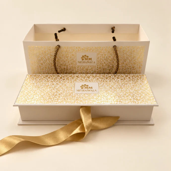 MM Mithaiwala White Cavity Hamper with golden patterns, a ribbon and a matching carry bag.